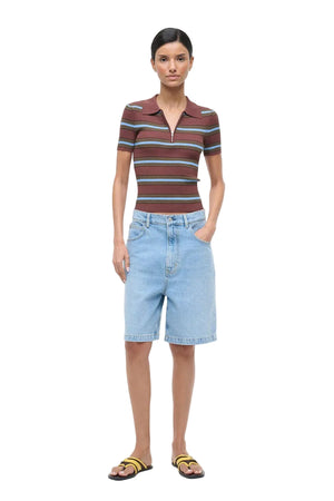 Woman wearing a striped polo shirt and denim shorts on a white background