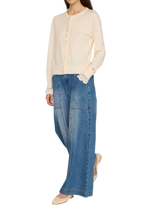A model wearing a cream-colored long-sleeve button-up cardigan with lace cuffs, paired with wide-leg blue denim jeans and beige pointed-toe flats, shown against a plain white background.