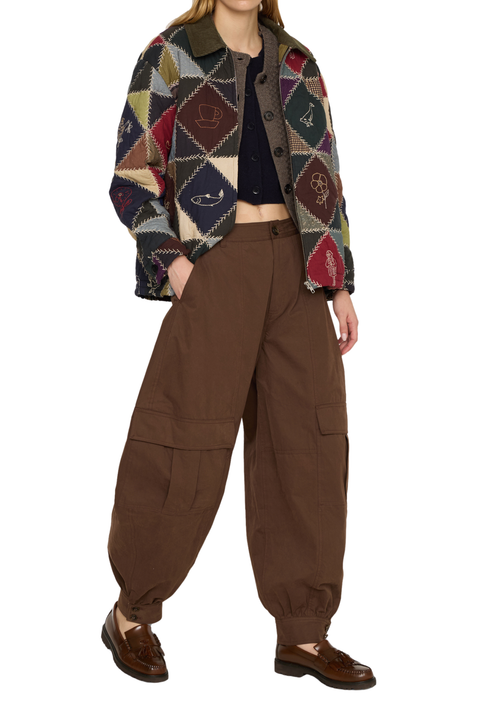 A model wearing a multicolor patchwork knit cardigan with geometric patterns, paired with brown baggy cargo pants and brown leather loafers, against a plain white background.
