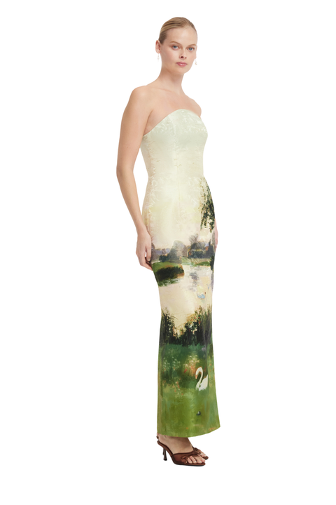 A strapless floor-length gown with a cream lace bodice and a printed scenic lower skirt featuring green fields, trees, water, and a white swan, shown on a model against a white background.