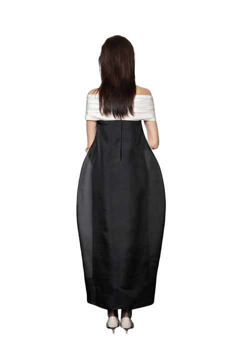 A woman viewed from the back wearing a long black off-the-shoulder dress with a white striped off-the-shoulder top, standing against a plain white background.