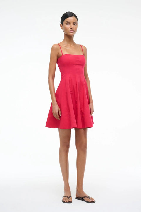 Side angle of a Woman wearing a red mini dress that features spaghetti straps and a straight neckline, corset style paneling, and an A-line skirt, paired with black sandals. 