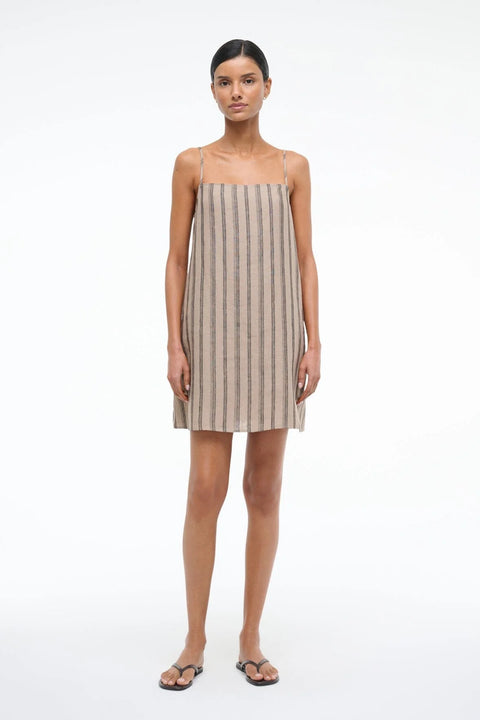 Woman wearing a mini shift dress with spaghetti straps, crafted from a brown striped linen, paired with brown sandals.