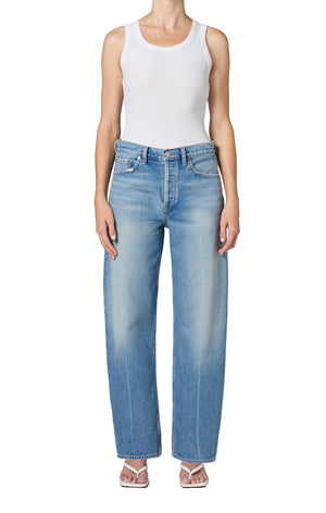 Person wearing a white tank top and light blue jeans on a white background