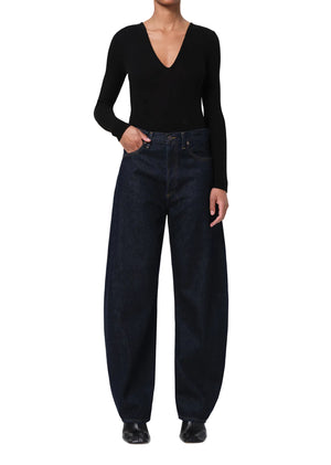 Person wearing a black long-sleeve top and dark blue, wide-leg jeans on a white background facing forward