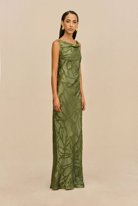 Woman wearing a green evening gown against a beige background standing to the side.