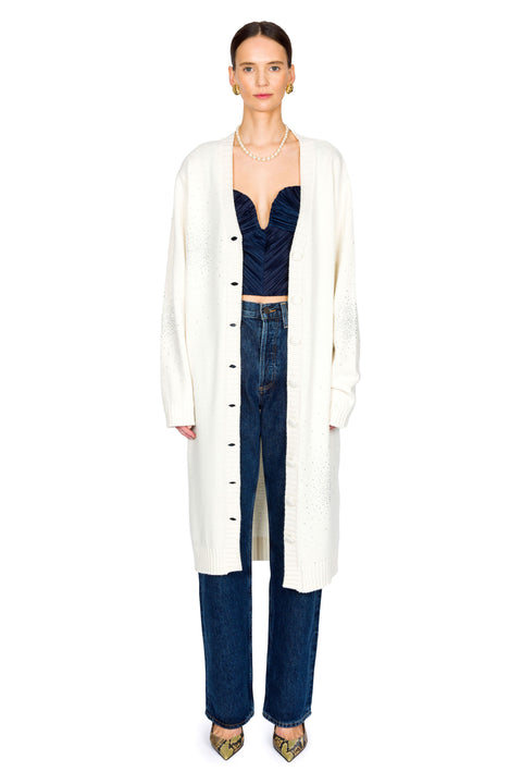 Woman wearing a long white cardigan over a dark top and jeans and pearl necklace on a white background
