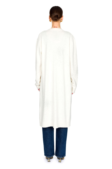 Person wearing a long white cardigan with crystal embellishments and blue jeans on a white background