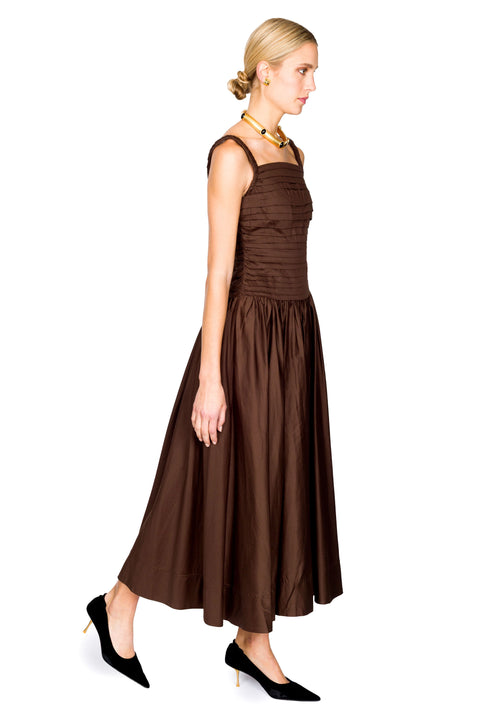 Woman walking to the right wearing a brown cotton maxi dress on a white background from the side