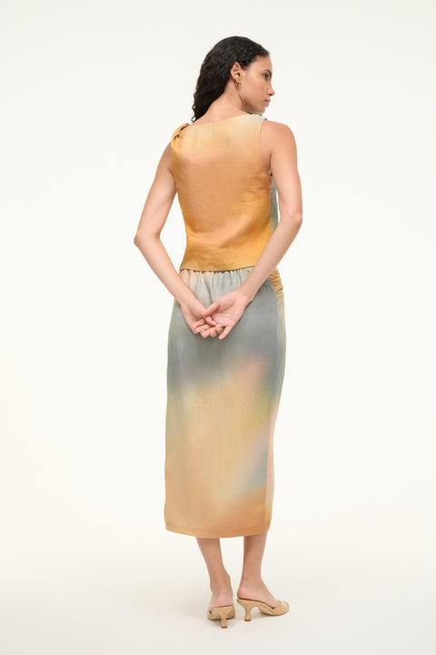 Back view of a woman wearing a pink, blue, green, and orange tie die tank top that is a boxy fit and features a twist detail on one shoulder, paired with a matching skirt. 