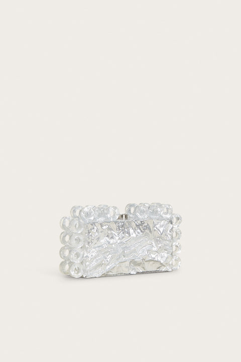 Side angle of a rectangular acrylic clutch that features a silver foil design and matching open circles of silver-foiled acrylic lining the shape of the clutch.