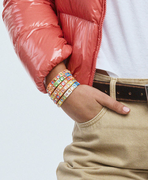 Models hand in pocket wearing multicolor enamel bracelets on wrist.