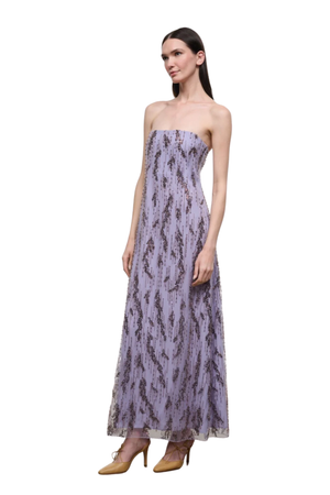 A woman modeling a strapless lavender maxi dress with a dark abstract print, paired with tan high heels, set against a plain white background.