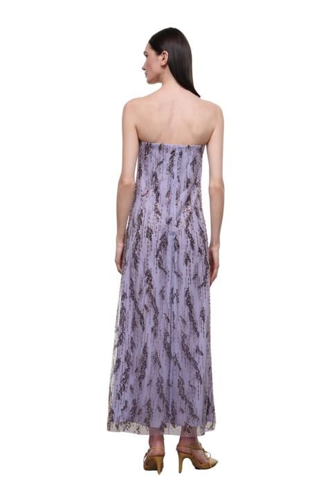 A woman shown from the back wearing a strapless lavender maxi dress with a dark abstract pattern, paired with brown high heels, against a plain white background.