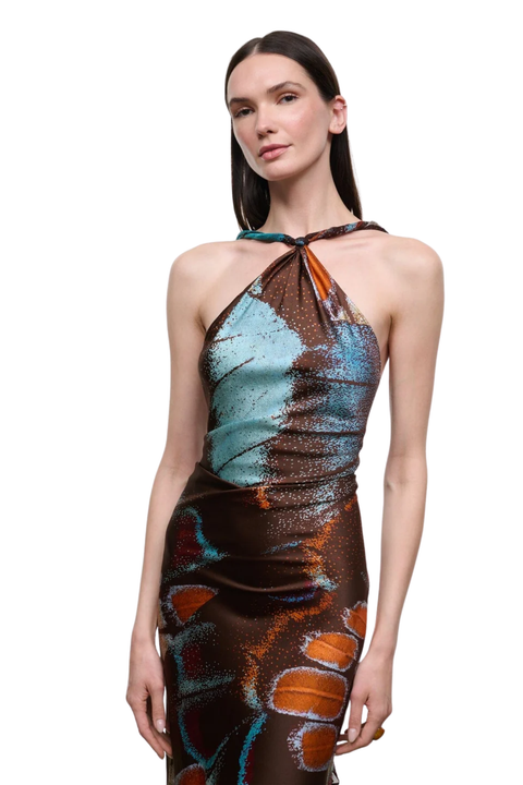 A model wearing a halter-neck dress with a metallic, abstract print in brown, teal, and orange, set against a plain white background.