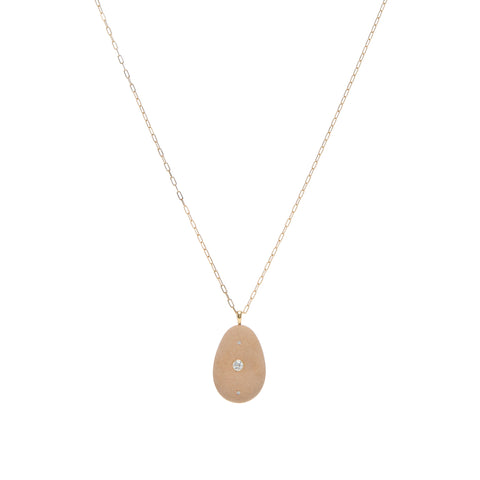 A tan, oblong stone pendant that is embellished by a round diamond in the center and accented by two small diamonds above and below, suspended on a yellow gold paperclip chain. 