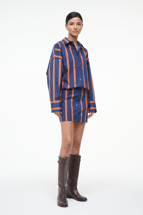 Side-facing woman wearing a blue and orange striped long sleeve mini dress with brown boots. 