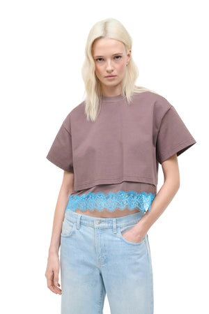 Woman wearing a brown cropped top with blue lace detail at the hem and light blue jeans with lace detailing.