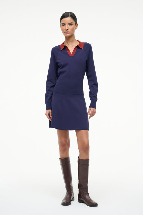 Woman wearing a navy dress with a red collar and brown boots on a white background