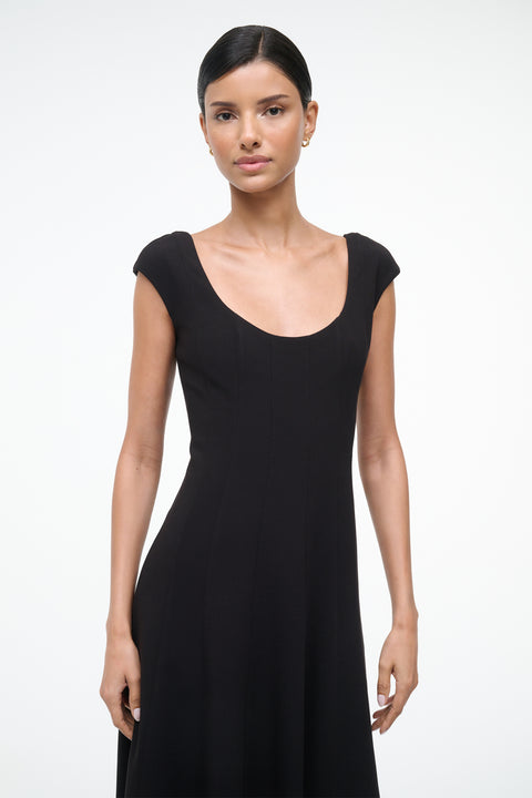 Close up of a woman wearing a black, A-line, midi dress that features a scoop neck, princess seams at the waist, and cap sleeves. 