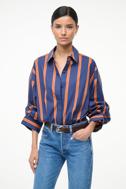 Close up of a woman wearing a blue and orange striped, long sleeve bodysuit with jeans and boots. 