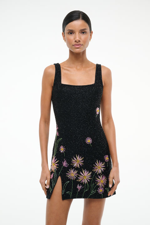 Close up of a woman wearing a sleeveless beaded mini dress that features a square neck and side slit, designed with pink dahlias on a black background. 