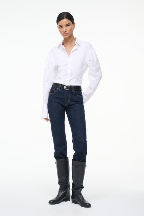 Woman wearing a white, long sleeve, button down shirt that features a tailored fit in the waist, paired with jeans and boots.