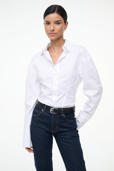Close up of a woman wearing a white, long sleeve, button down shirt that features a tailored fit in the waist, paired with jeans.