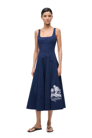 Woman wearing a navy blue dress with white embroidery on a white background