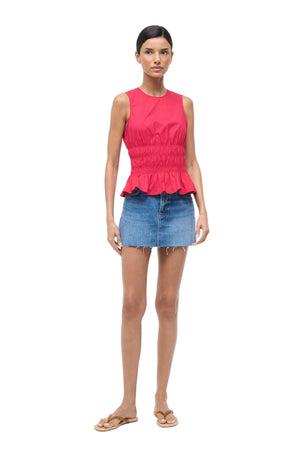 Woman wearing a red sleeveless top and denim skirt on a white background