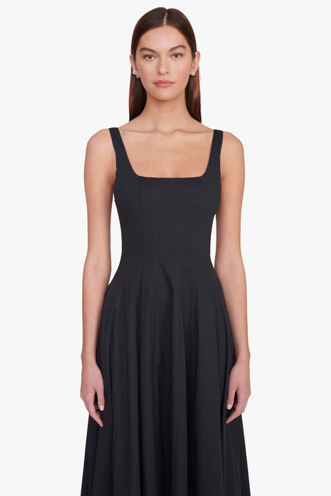 Close up of a woman wearing a sleeveless, black maxi dress that features a square neck, corset style paneling, and A-line skirt. 