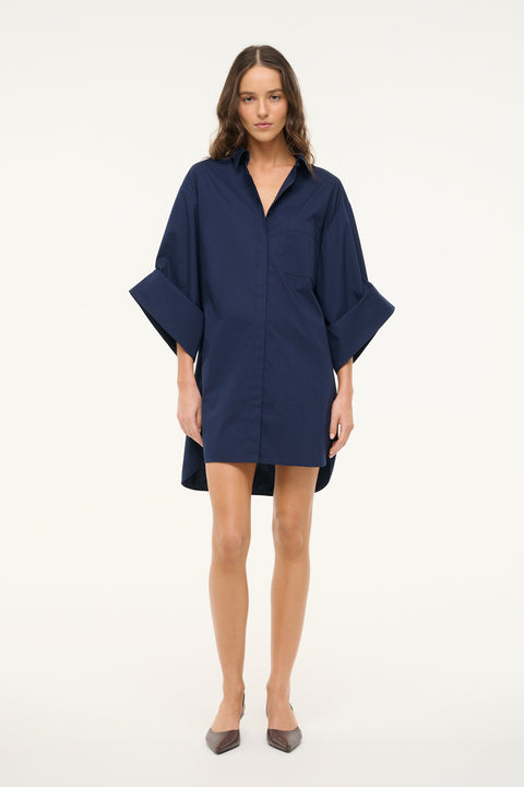 Woman wearing a navy shirt dress that features a 3/4 length cuffed sleeves, collar, and button down detail, paired with brown slingbacks. 
