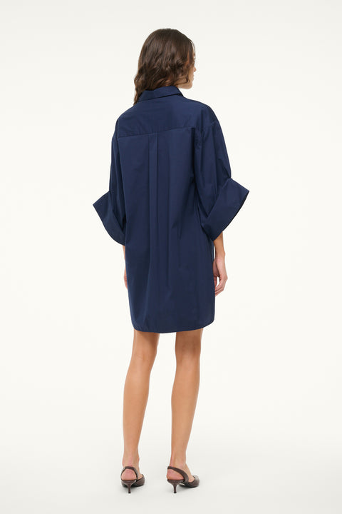 Back view of a woman wearing a navy shirt dress that features 3/4 length cuffed sleeves, collar, and button down detail, paired with brown slingbacks. 