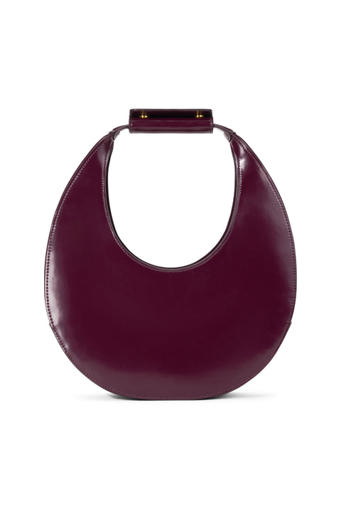 A deep maroon, patent leather top handle bag inspired by the shape of a crescent moon. 