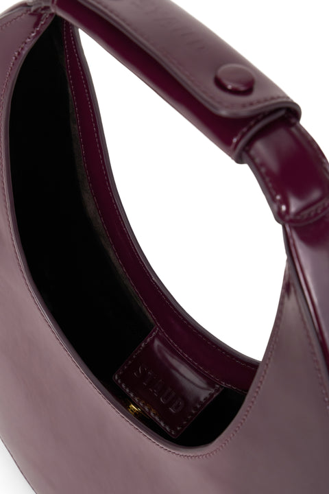 Inside of a deep maroon, patent leather top handle bag inspired by the shape of a crescent moon with a snap closure.