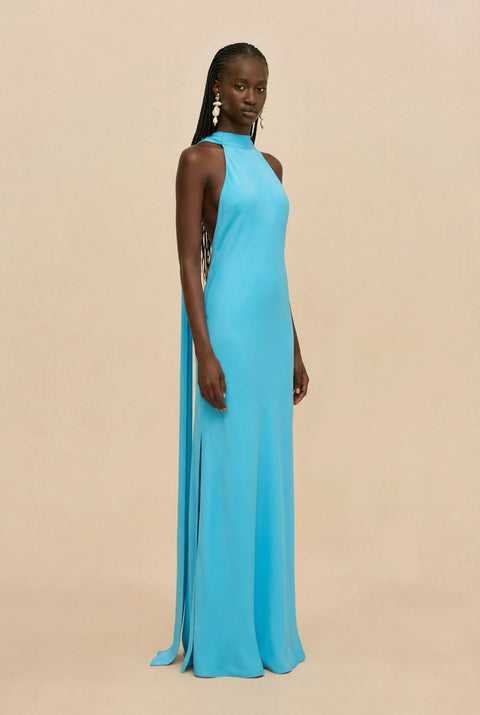 Woman wearing a blue halter neck gown on a beige background standing to the side.