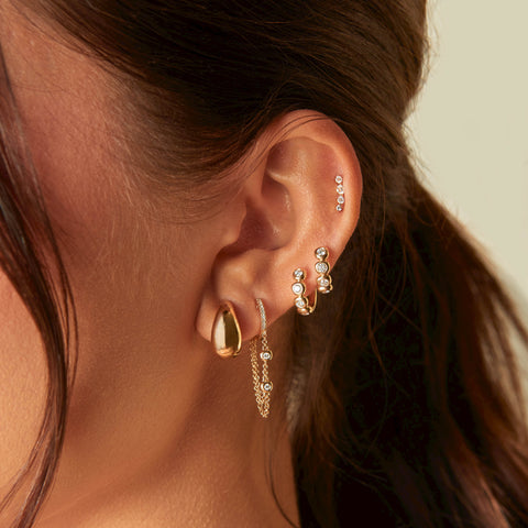 Close-up of an ear wearing gold and diamond earrings with a neutral background