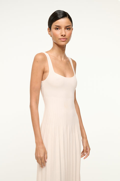 Close up of a woman wearing a cream knit midi dress that features a ribbed bodice and pleated skirt. 