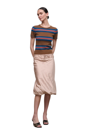 A woman modeling a brown short-sleeve knit top with blue, red, and white horizontal stripes, paired with a beige satin midi skirt and black heeled sandals, against a plain white background.