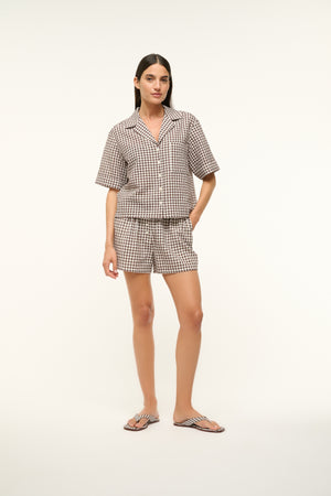 Woman wearing a brown gingham, short-sleeve button-up shirt with matching shorts