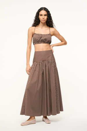 Woman wearing a cropped bubble top that is brown with white pinstripes, paired with a matching maxi skirt. 