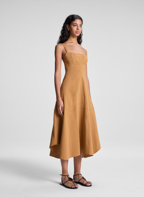Woman turned to side wearing a mustard brown dress against a white background