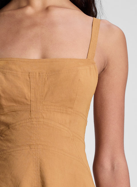 Close-up of a mustard brown dress  with thin straps on a person against a white background