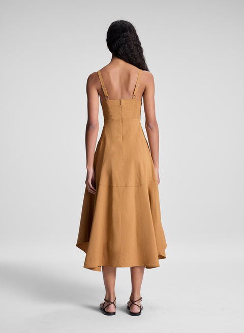 Woman facing away wearing a mustard brown dress with a plain background