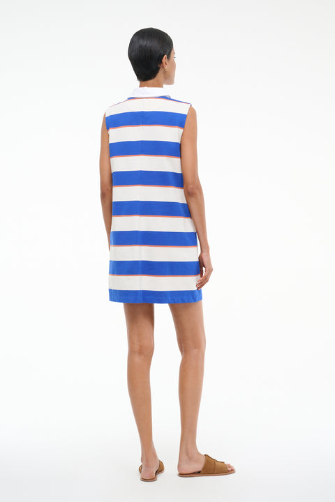 Back-facing Woman wearing a sleeveless mini dress that features a blue and white stripe pattern with thin orange stripes with a white contrast collar, paired with brown sandals. 