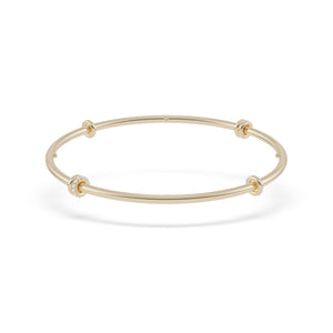 Ghost image of a thin yellow gold bangle that features six yellow gold annulets, one pave with diamonds. 