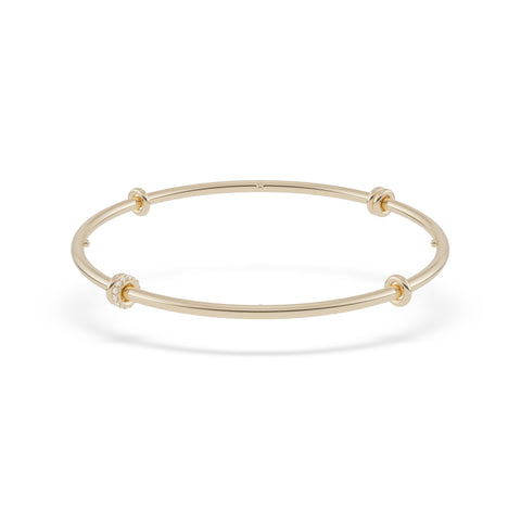 Ghost image of a thin yellow gold bangle that features six yellow gold annulets, one pave with diamonds. 