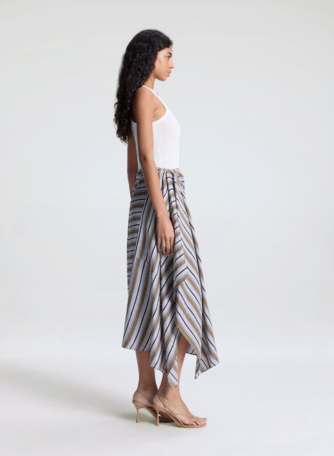 Woman facing the right wearing a white top and striped midi skirt on a white background.