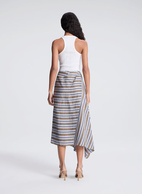 Woman turned to the back wearing a white top and striped multi colored midi skirt on a white background