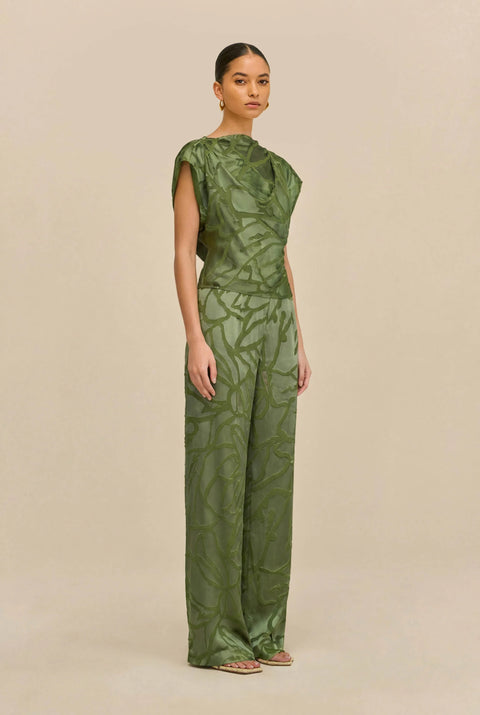 Woman wearing a green matching top and wide leg pant against a white background standing to the side.